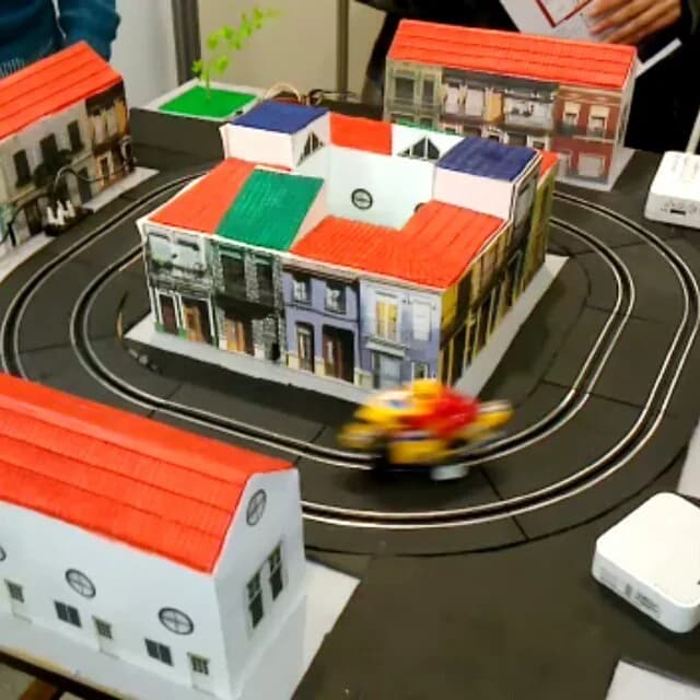 Maqueta física en funcionamiento con edificios y un vehículo sobre un circuito